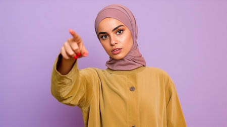 Positive good looking Muslim lady points on top reacts on awesome promo copy space shows something incredible dressed in traditional clothing isolated over purple backgro : Generative AIの素材