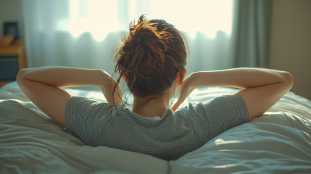 Relaxed young woman sitting on bed at home in the morningの素材