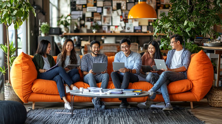 Group of diverse business people sitting on orange sofa and working on laptopの素材