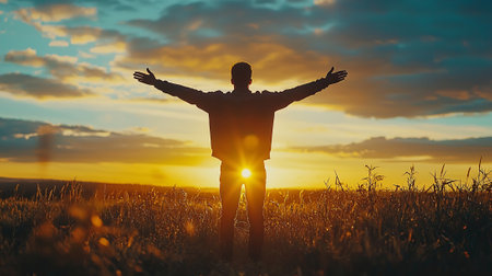 Man with arms outstretched standing in field at sunset. Freedom conceptの素材