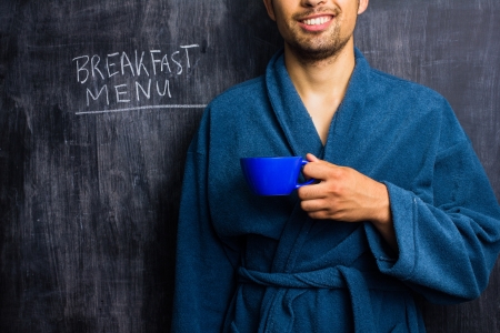 Man in dressing gown in front of blackboard with breakfast menu written on itの写真素材