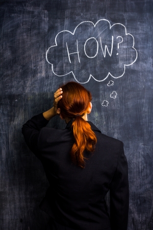 Redhead businesswoman at blackboard asking howの写真素材