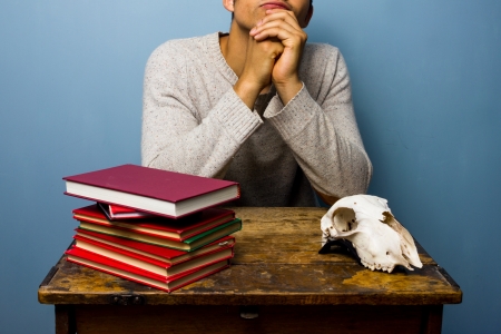 Thinking man at desk with books and goat s skullの写真素材