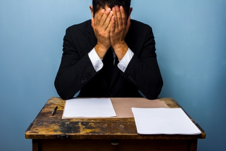 Worried businessman sitting at an old desk with documents in front of himの写真素材