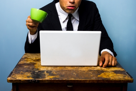 Shocked businessman nearly spilling coffee on his laptop computerの写真素材