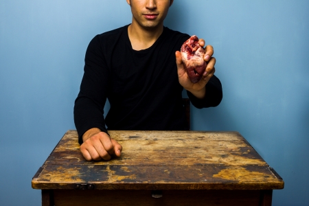 Young man is holding a raw animal s heartの写真素材