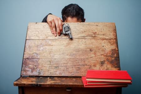 Student with a gun looking inside an old school deskの写真素材