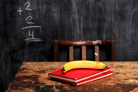 Stack of books and banana on desk by blackboardの写真素材