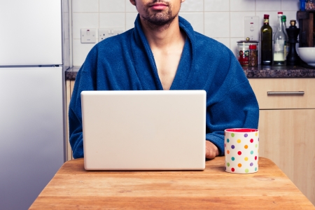 Man in robe is working on laptop and drinking coffeeの写真素材