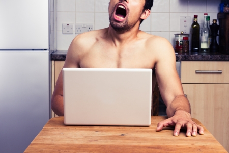 Naked young man is watching pornography on his laptopの写真素材