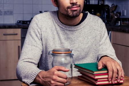 Young man with two empty jars and stack of booksの写真素材