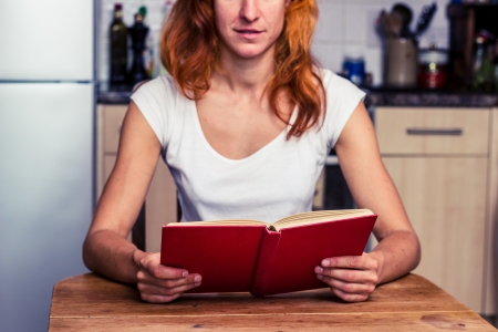 Young redhead woman sitting in kitchen and readingの写真素材