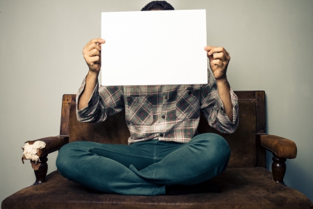 Young man on old sofa holding up a blank signの写真素材