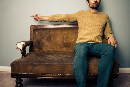 Young man on vintage sofa is pointing leftの写真素材