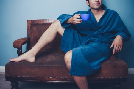 Man in bathrobe is sitting on sofa and drinking coffeeの写真素材