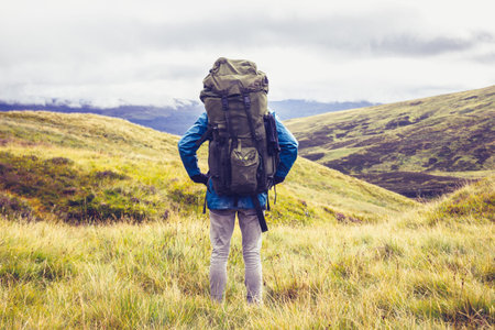 Hill walker with big backpack is standing in the middle of wilderness