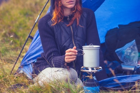 Young woman is camping and cooking on a portable stoveの写真素材