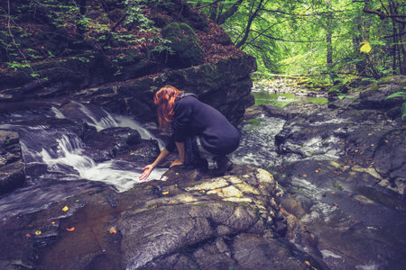 Young woman admiring flowing water in forestの写真素材