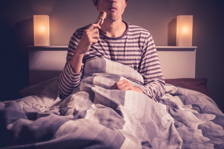 Young man eating chicken in bed