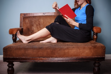 Young woman sitting on sofa and reading a bookの写真素材