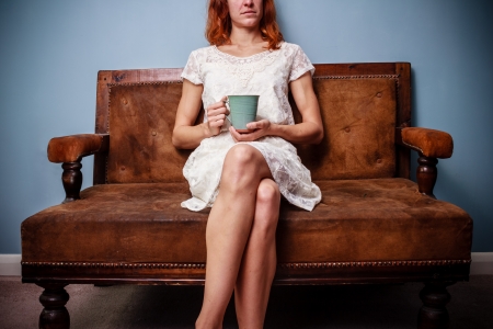 Young woman in white dress sitting on sofa drinking teaの写真素材