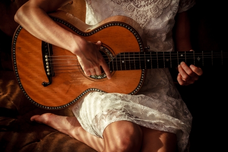 Young woman is sitting on sofa playing guitar, shadows on her skinの写真素材