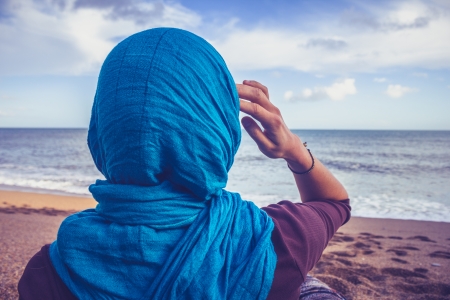 Young woman in headscarf on the beach is looking at the seaの写真素材