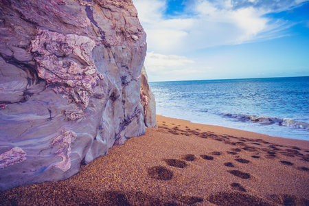 Footprints on the beach by a cliff on a sunny day
