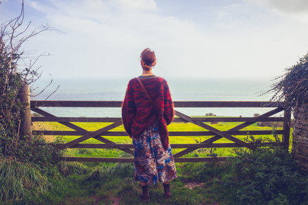 Young woman standing at gate and admiring sea and rural landscape