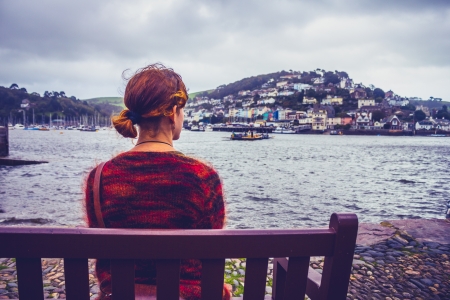 Young woman sitting on bench and admiring harbor townの写真素材