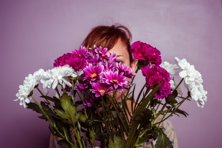 Young woman hiding behind a bouquet of colorful flowersの写真素材