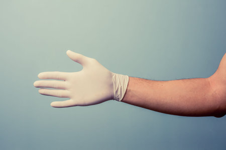 Hand wearing a latex surgical glove is extended for a handshakeの写真素材