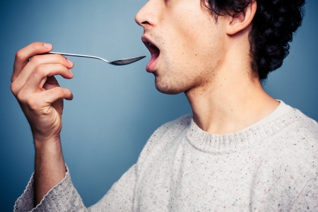 Young man is feeding himself a spoonful of medicineの写真素材