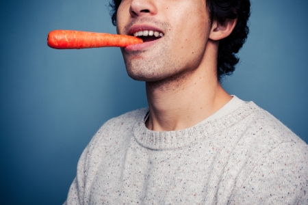 Young man is eating a carrotの写真素材