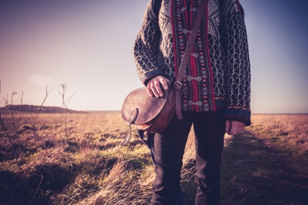 Young woman with shoulder bag standing in a field at sunsetの写真素材