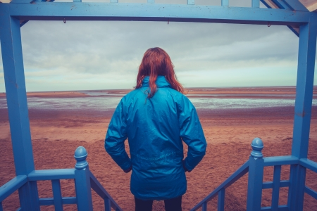 Rear view of woman standing on porch looking at coastの写真素材