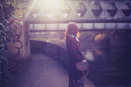 Young woman looking at canal and bridge at sunsetの写真素材