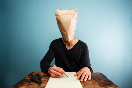 Man with bag over head writing suicide noteの写真素材
