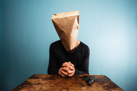 Praying man with a paper bag over his head at deskの写真素材