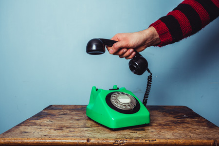 Man s hand lifting receiver of old rotary phoneの写真素材