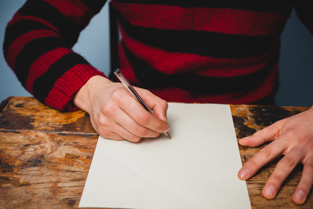 Young man sitting at a desk and writing letterの写真素材