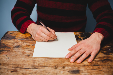 Young man sitting at a desk and writing letterの写真素材