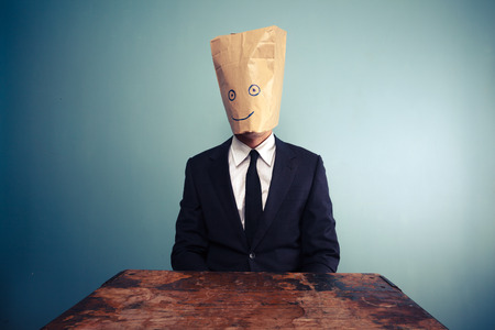 Businessman with bag over his head relaxing at deskの写真素材
