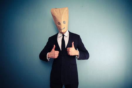 Businessman with paper bag over head giving thumbs upの写真素材