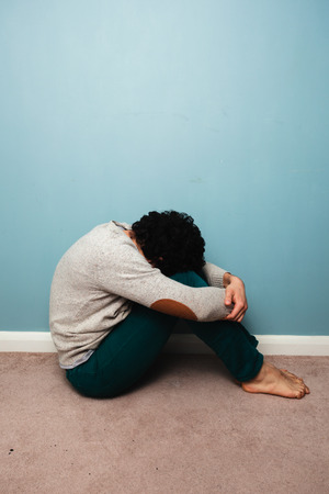 A sad young man in sitting on the floor against a blue wallの写真素材
