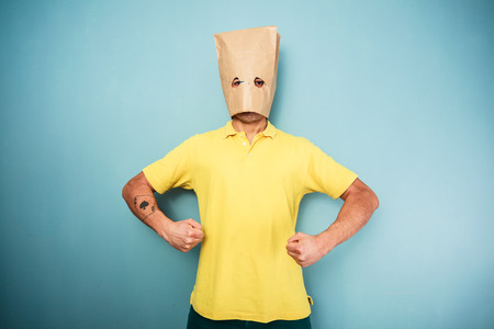 Young man with a bag over his head standing with his arms flexedの写真素材