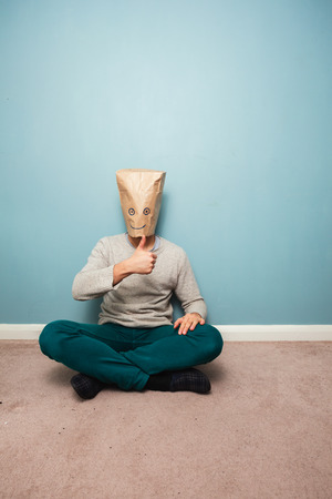 Man with a bag over his head is sitting on the floor and giving thumbs upの写真素材