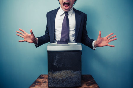Businessman has got his tie stuck in a paper shredderの写真素材