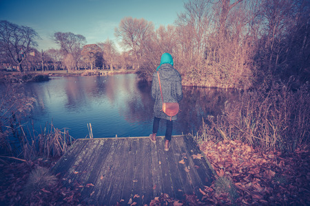 Young woman standing by a pond in park in autumnの写真素材