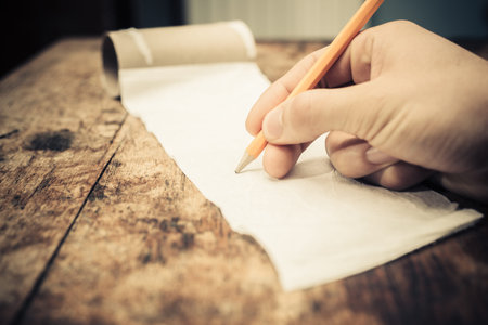Closeup on a man's hand writing on toilet paper with a pencil